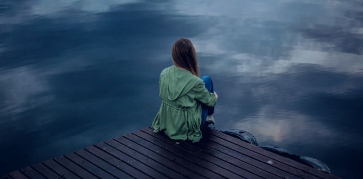 A depressed woman sitting on a dock looking over a lake