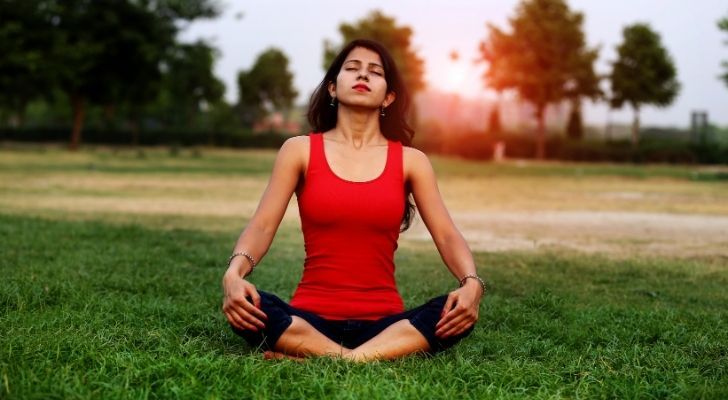 A woman breathing deeply sitting on the grass with her legs crossed