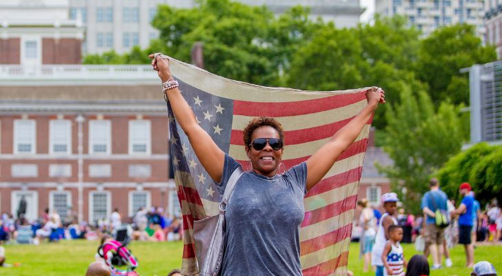 A person holding the US flag at a park.