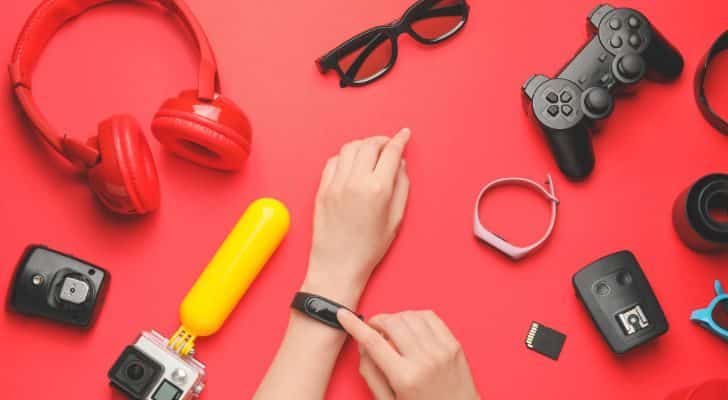 Various electronics and gadgets are laid on a table as a person tries on a smart watch