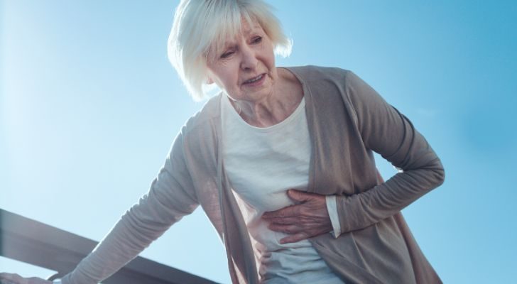 An old lady leans on a table for support while catching her breath