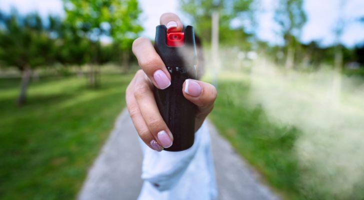 A hand holding a can of pepper spray while spraying it