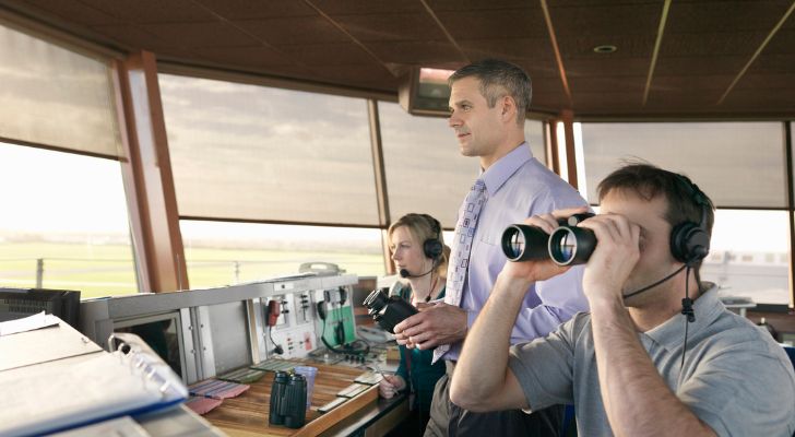 Three air traffic controllers look out over an airport