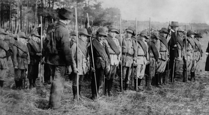 A group of young boys forms lines and holds sticks as they practice for being in the army