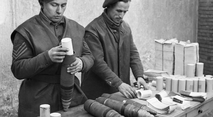 Two men pack rolls of propaganda leaflets into shells to be dropped from planes