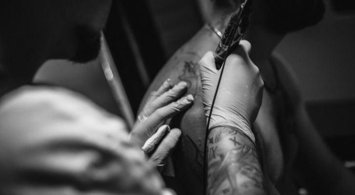 A man with a glove on tattooing someone