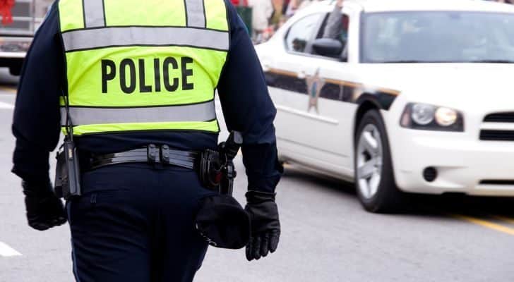 A man in a police uniform with a high visibility jacket saying "police" walks down a street