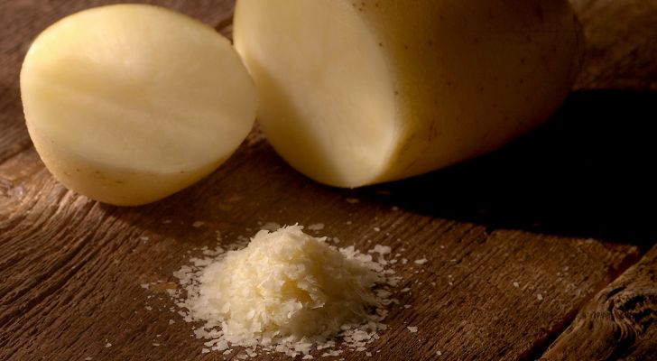 Two cut pieces of potato on a wooden table alongs side some flakes from the potato