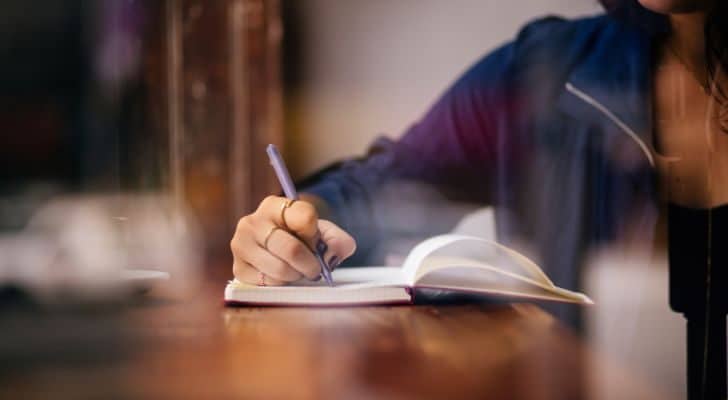 A hand writes in a book on a desk