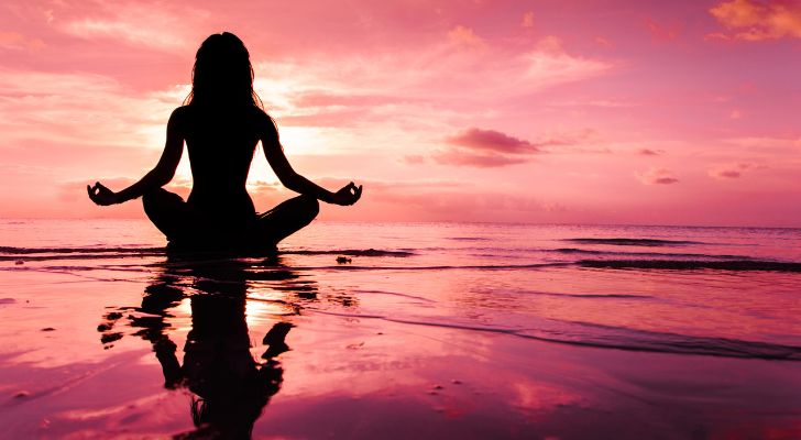 A woman meditating on a beach at sunset