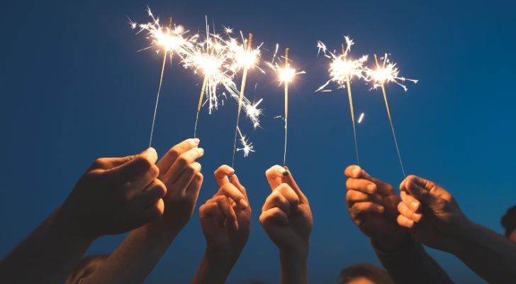 Several hands hold up sparklers at night