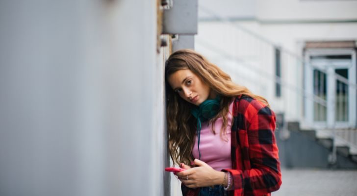 A girl on her phone leaning against a wall