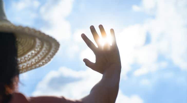 A woman in a summer hat holding her hand up to the heat of the sun