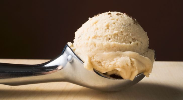 An ice cream scooper holding a pale yellow scoop of ice cream