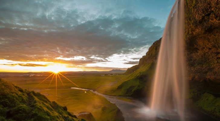 Seljalandsfoss Waterfall in Iceland pours into a valley while the sun touches the horizon in the distance