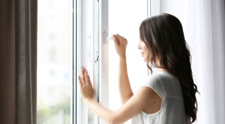 A woman opening a window as natural daylight fills the room