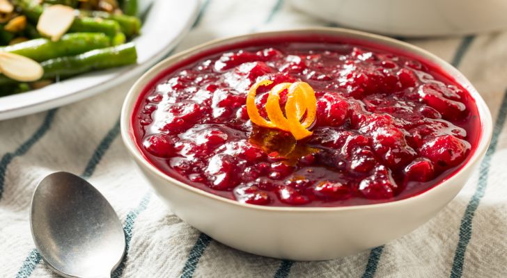 A bowl of cranberry sauce is topped with a curl of orange peel