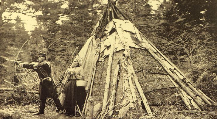 Mi'kmaq people standing next to a teepee in a forest