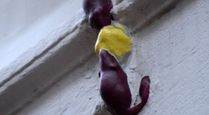 A small statue built into a wall of two mice fighting over a piece of cheese