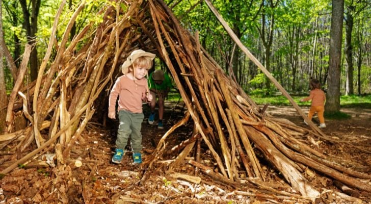 A child playing in the woods in a small shelter built out of sticks