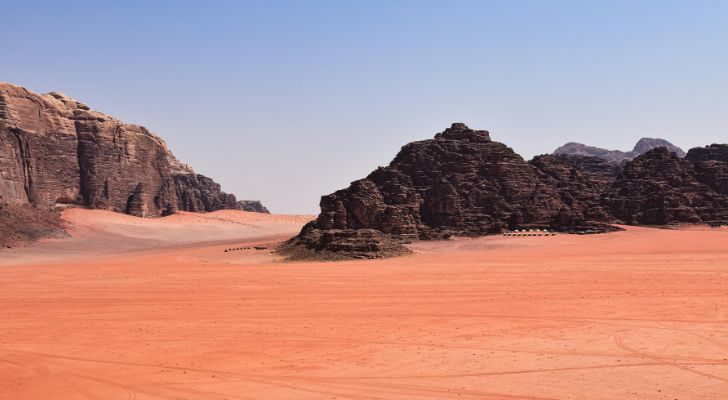 Large black rocks sticking out of vast orange sands in Jordan's Black Desert