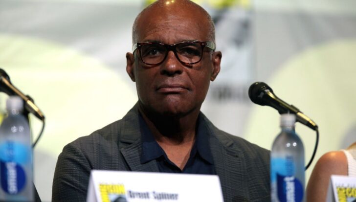 Michael Dorn sitting at a panel with a microphone and bottled water in front of him