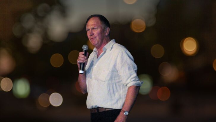 Vaughn Armstrong holding a microphone with a blurred background of lights