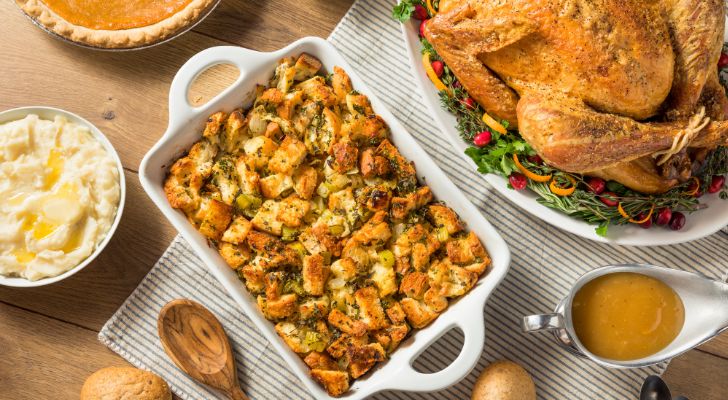 A baking tray of stuffing is placed on a table next to a roast turkey