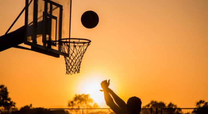 A man jumping and shooting a basketball at a basketball hoop during sunset