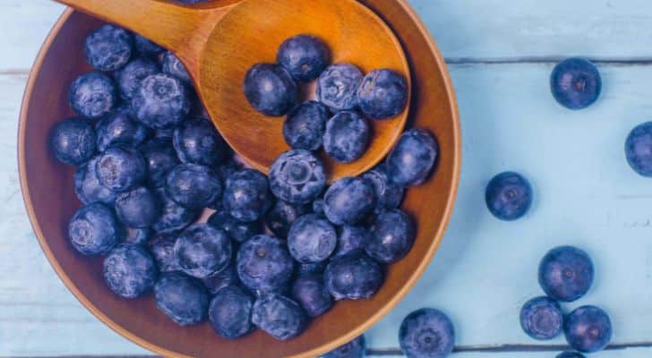 A wooden bowl and spoon, both filled with blueberries