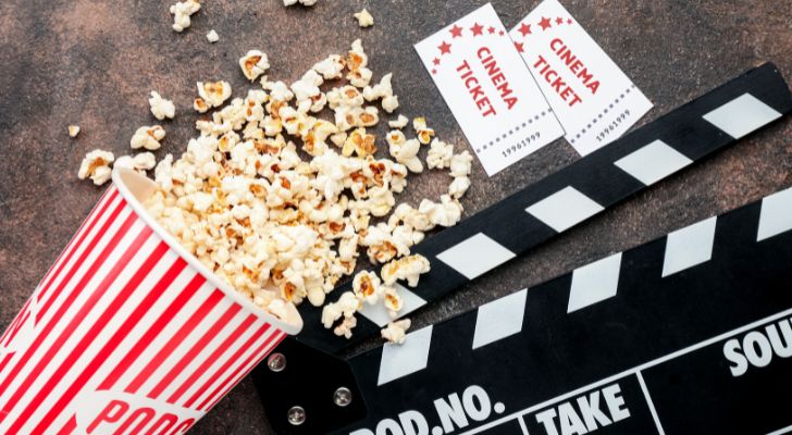 Two cinema tickets next to a clapperboard and a bucket of popcorn