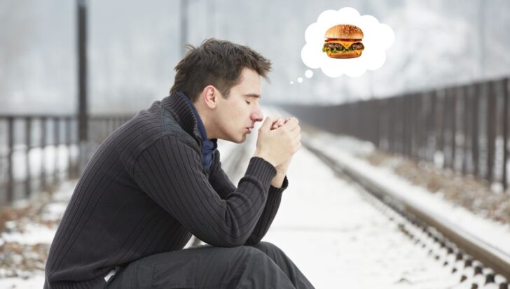 Person sitting on a snowy path with a thought bubble showing a hamburger