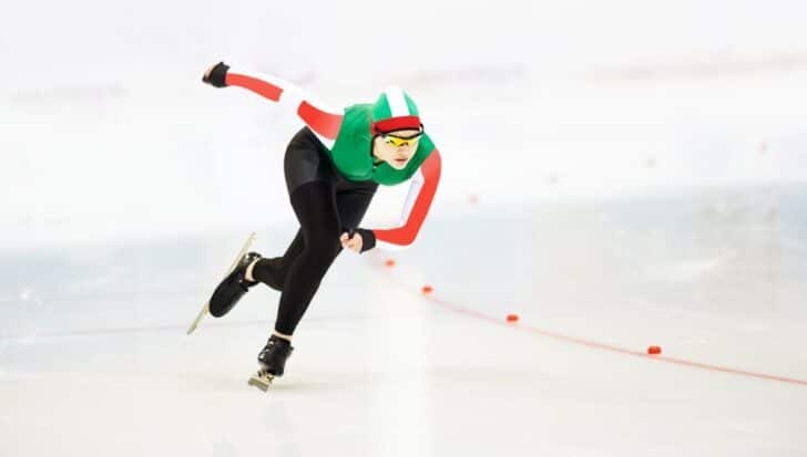 A speed skater in a green, red, and white uniform gliding on an ice rink