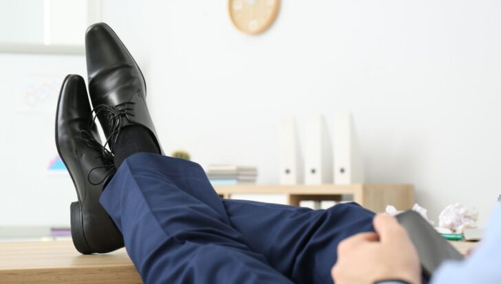 Person in business attire lounging with feet on a desk in an office setting, implying reduced productivity