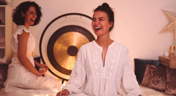 Two women in white sit and laugh during a yoga session