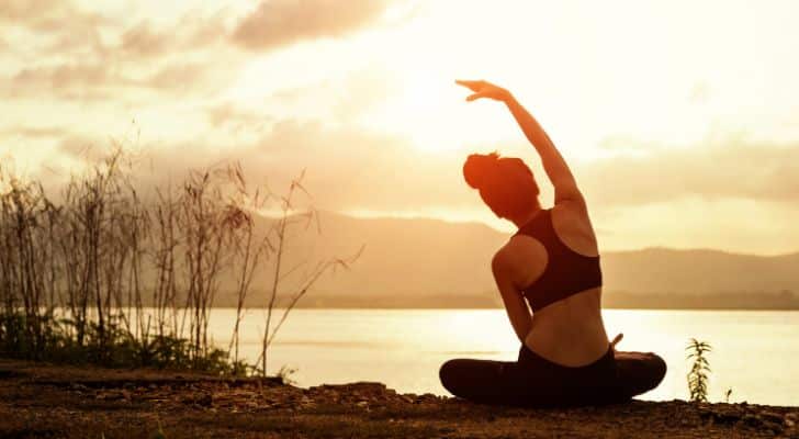 A woman sitting and stretching in a yoga pose by a laake