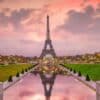 The Eiffel Tower at sunset with a reflection in a pond, surrounded by gardens and trees