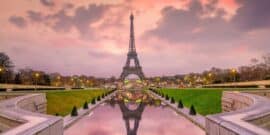 The Eiffel Tower at sunset with a reflection in a pond, surrounded by gardens and trees