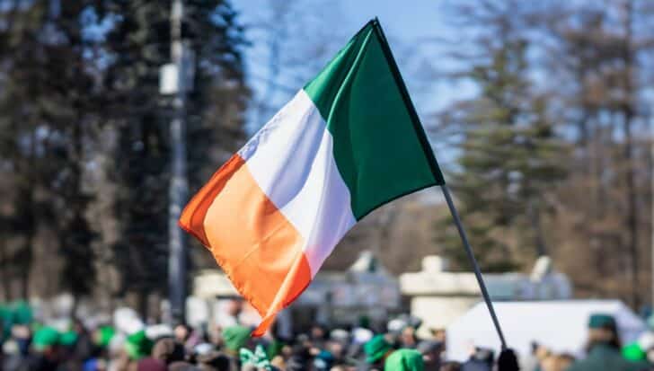 Irish flag waving with a crowd of people in the background, during a St Patrick's Day celebration