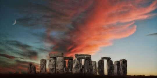 Stonehenge with a dramatic sunset sky and a crescent moon