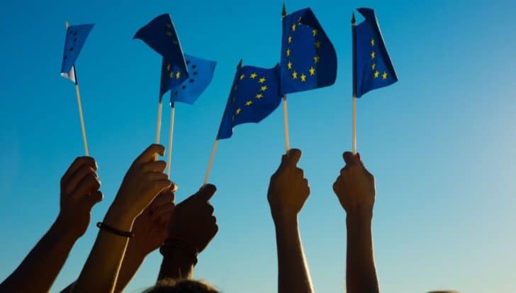 Hands raising blue flags with yellow stars symbolizing the European Union