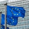 European Union flags waving in front of a modern glass building