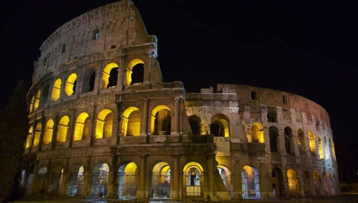 The Colosseum at night, illuminated by lights highlighting its arched structure and ancient architectural details