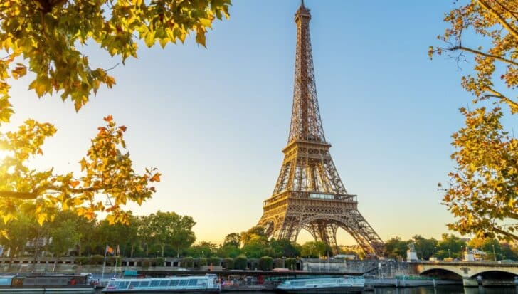 The Eiffel Tower surrounded by trees and boats on the Seine River at sunset