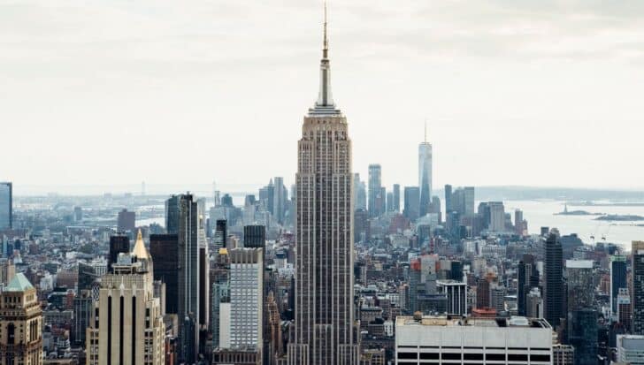 The Empire State Building stands prominently among the New York City skyline with other skyscrapers and a distant view of the water
