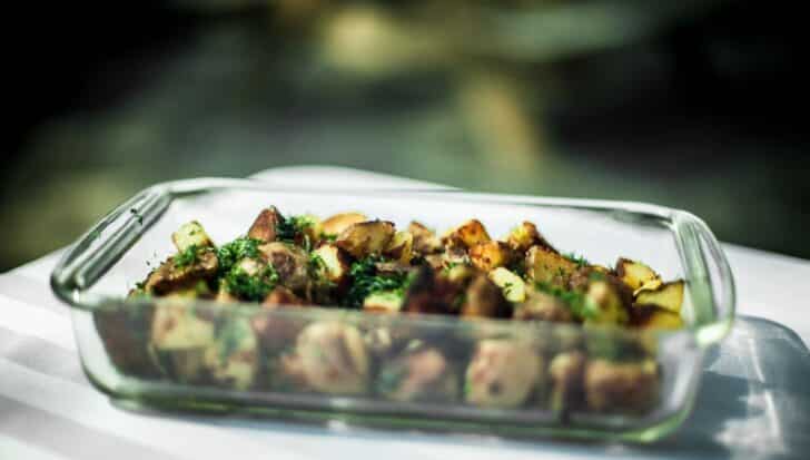 A pyrex glass dish containing roasted potatoes with herbs