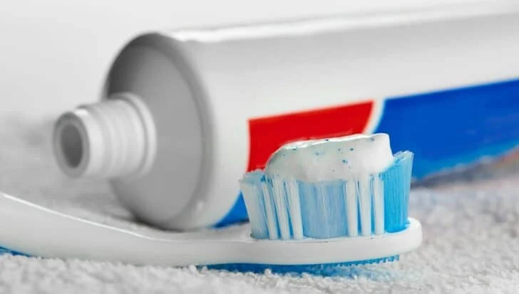 A toothbrush with toothpaste on the bristles next to an open toothpaste tube