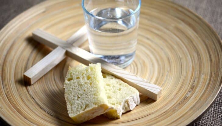 A wooden cross, a glass of water, and slices of bread on a round wooden plate, symbolizing Lent and the Holy Week of Easter