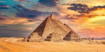 The Pyramids of Giza under a colorful sunset sky with a sandy foreground