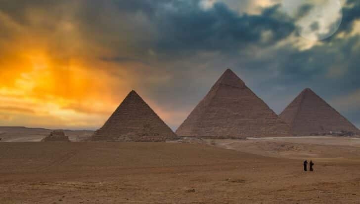 The Pyramids of Giza under a dramatic sky with two people in the foreground